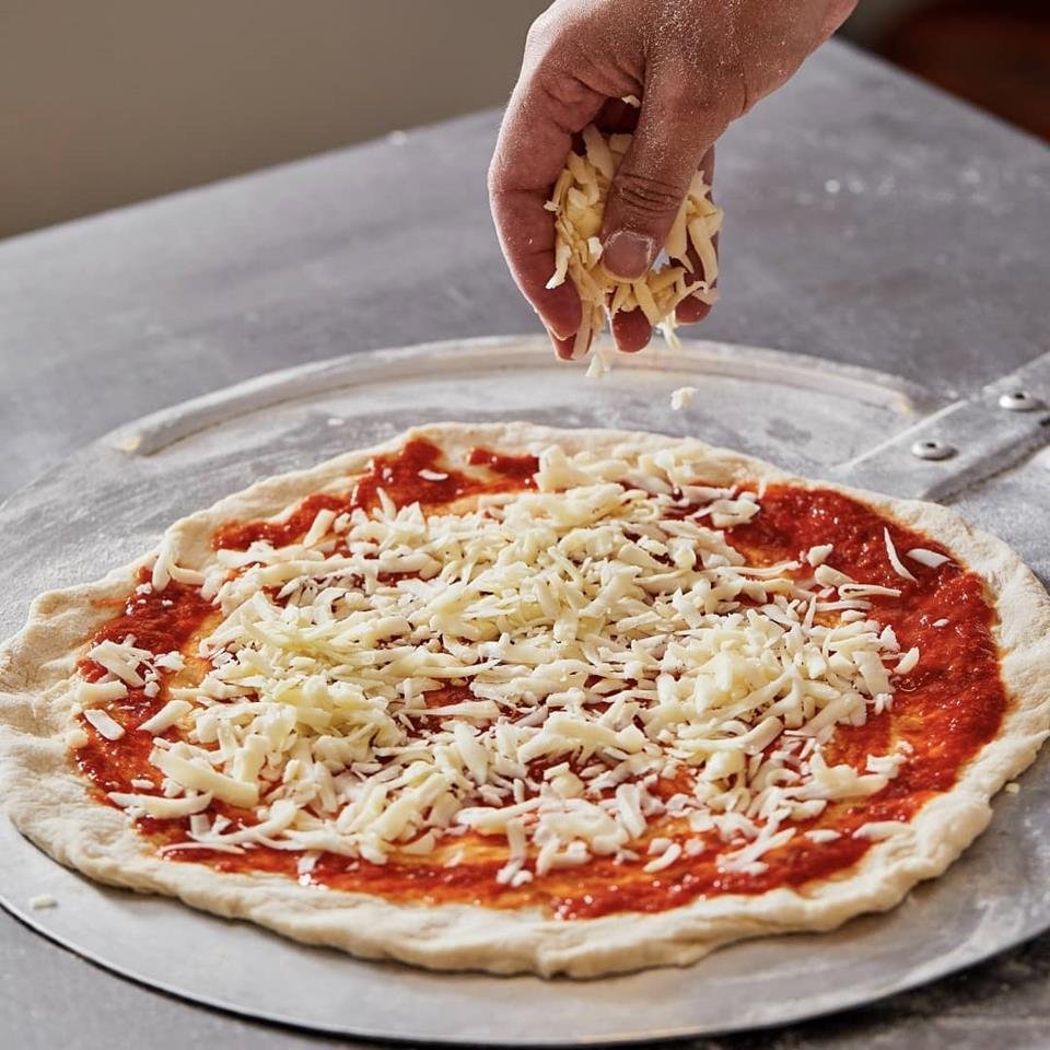 na foto vemos uma massa de pizza aberta com molho de tomate e queijo ralado