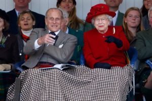Foto colorida. Príncipe Philip e rainha Elizabeth sentados com um pano sobre as pernas