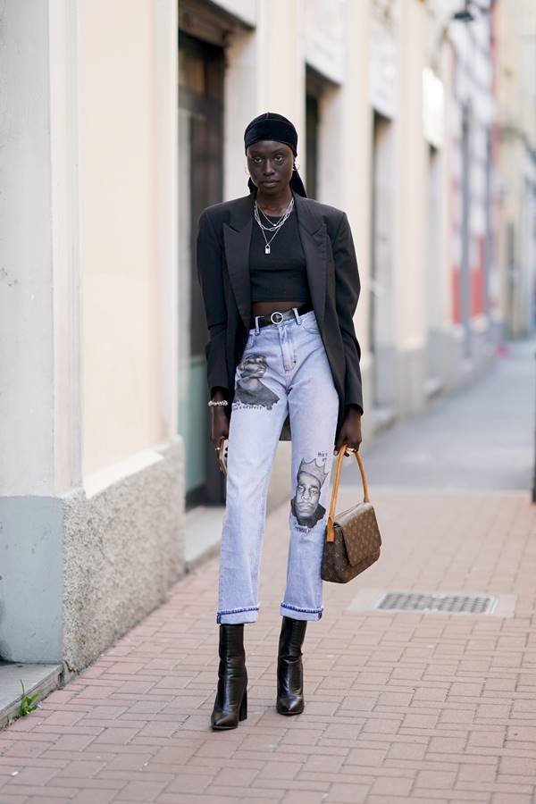 Mulher preta posando para foto na rua, com calça jeans e bolsa de mão