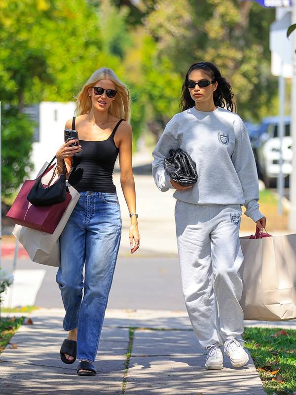 Duas mulheres brancas andando na rua com sacolas de compras nas mãos
