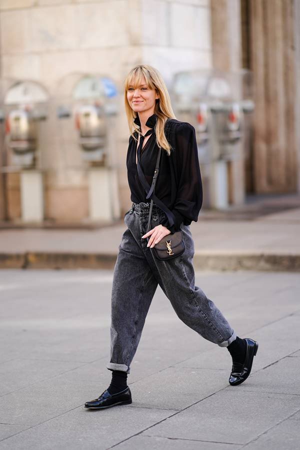 Mulher branca andando na rua com calça jeans preta e camisa social na mesma cor