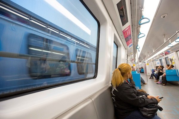 Imagem de mulher, vestindo tons escuros, sentada em um vagão do metrô - Metrópoles
