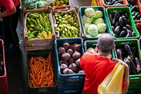 Consumidor escolhe verduras de caixas na Ceasa, no DF, segurando sacola amarela nas costas - Metrópoles