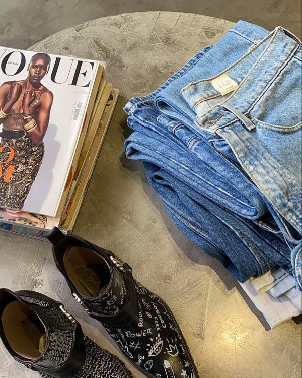 Calças jeans vintage em cima de uma mesa ao lado de revistas Vogue e uma bota estilo cowboy