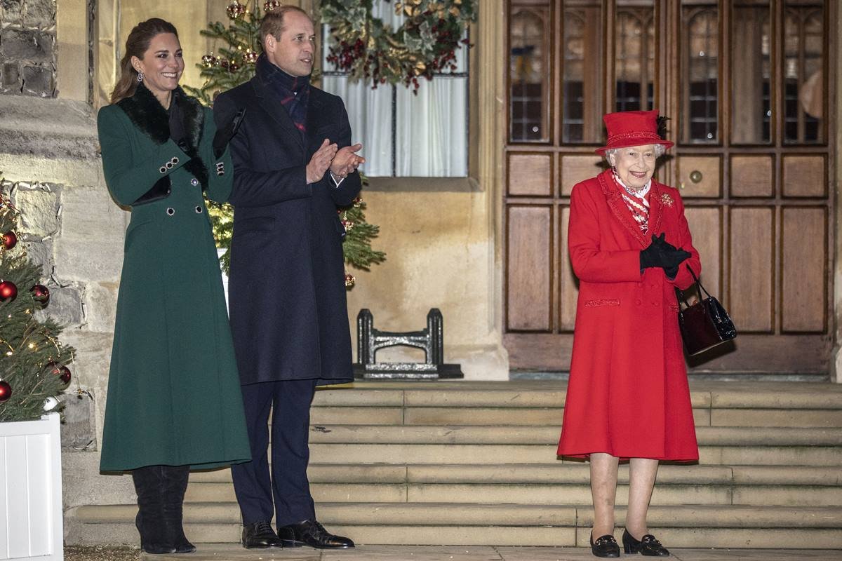 Foto colorida. Kate Middleton, príncipe William e rainha Elizabeth em frente a uma escada