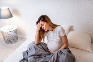 Mulher grávida sentada na cama colocando a mão na cabeça