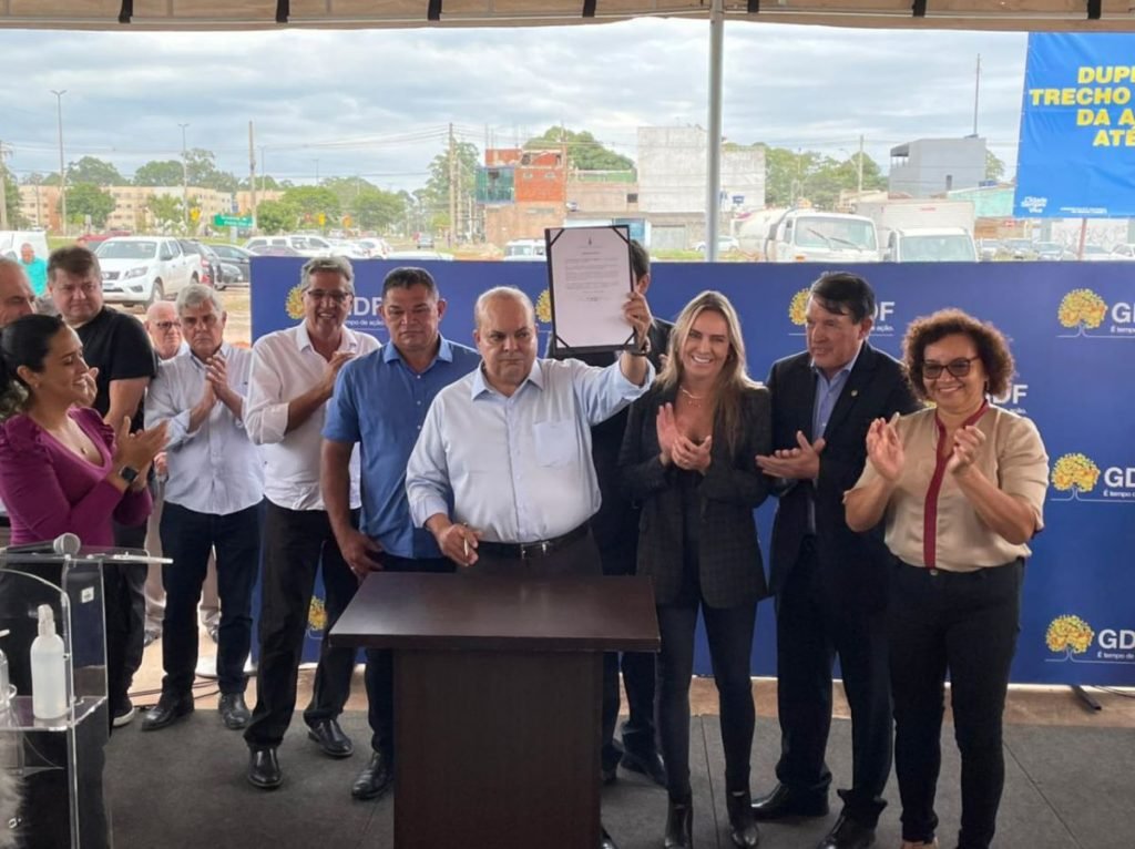 Ibaneis, governador do DF, participa de abertura de obra para duplicação de rotatória no Riacho Fundo ao lado de outras autoridades, diante do público e imprensa. Ele levanta papel assinado - Metrópoles
