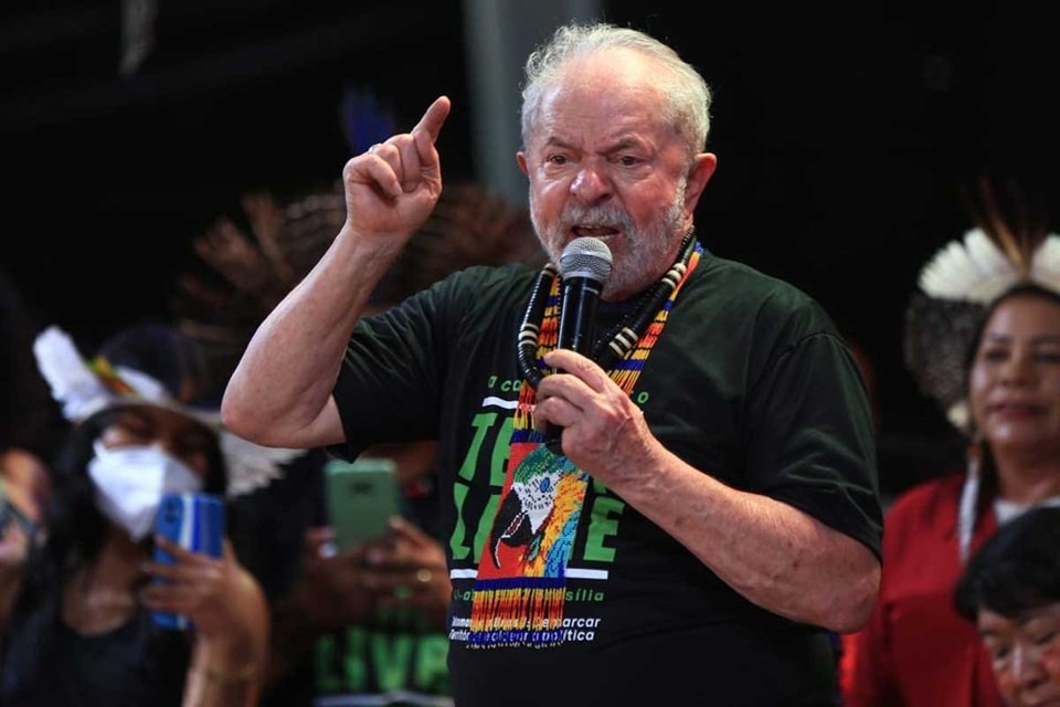 O ex-presidente Lula discursa em acampamento indígena Terra Livre, em Brasilia, cercado por lideranças de diferentes etnias. Ele segura um microfone e gesticula - Metrópoles
