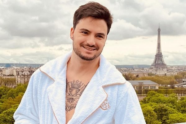 O youtuber Felipe Neto posa para foto e sorri usando um roupão branco na sacada de hotel de luxo em Paris. Ao fundo, é possível ver a torre Eiffel - Metrópoles