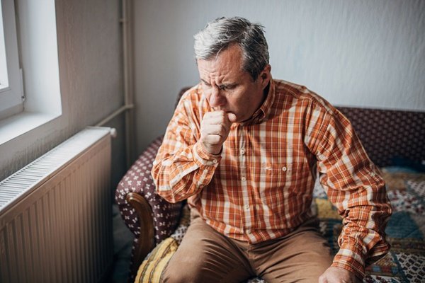 Man sitting coughing.  He has gray hair and wears a checkered shirt - Metrópoles