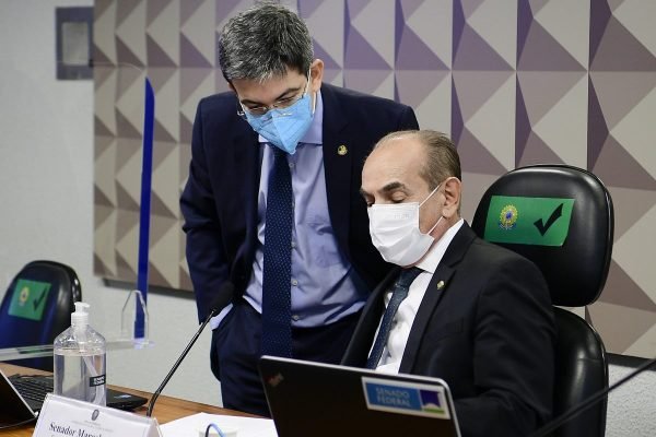 O senador Randolfe Rodrigues se abaixa próximo à mesa diretora da Comissão de Educação, onde o presidente Marcelo Castro se senta. Ambos olham para folhas de papel - Metrópoles