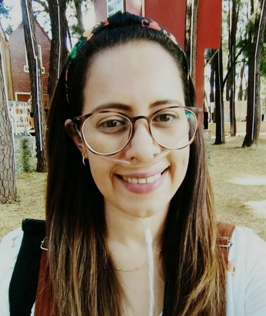 Mulher com cabelos grandes, óculos e tubos de soro no nariz sorrindo