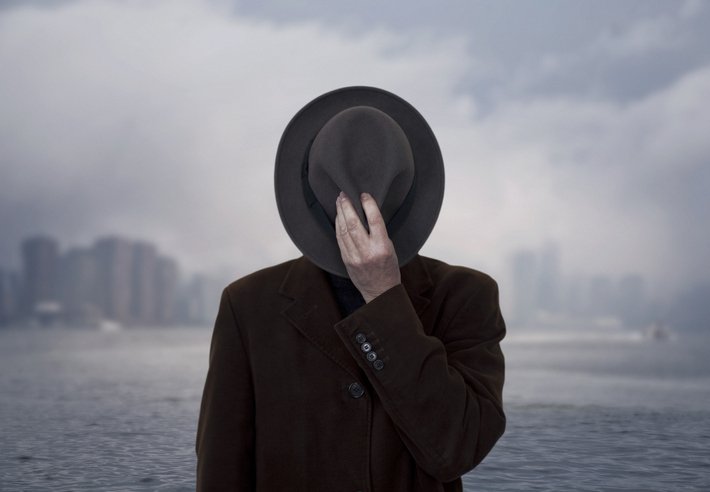 A man in a long brown coat with a hat in front of his face is METROPOLIS