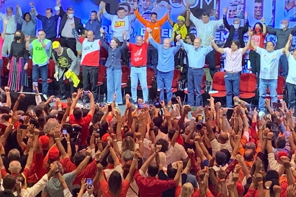 Lula inagura agenda política com Alckmin em encontro com as centrais sindicais. Na foto, eles seguram as mãos levantadas com outras figuras políticas diante de uma plateia que também ergue os braços - Metrópoles