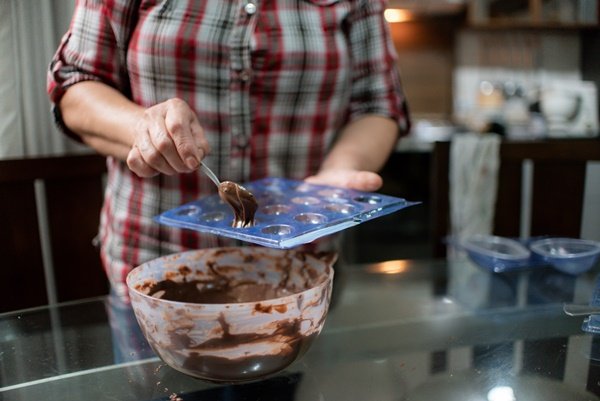 mulher fazendo chocolate artesanal. ela tem nas mãos uma forma e uma colher