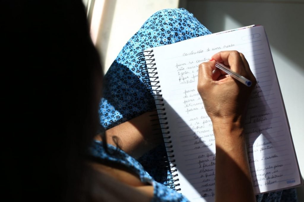 Mulher aparece na imagem escrevendo em caderno