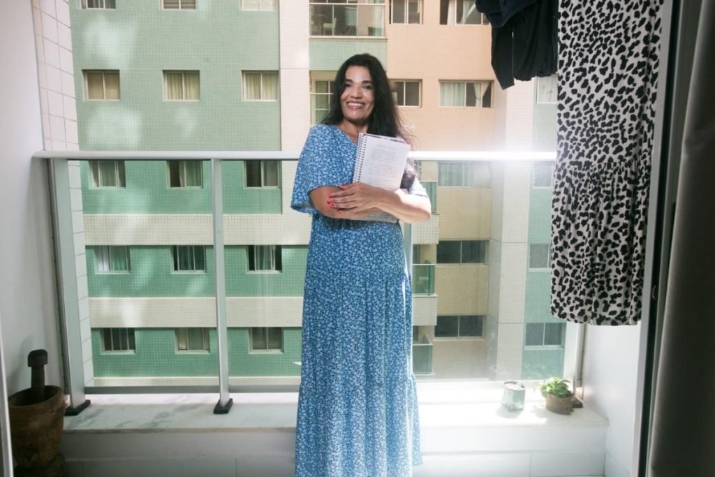 Mulher aparece em pé com um caderno nas mãos-Metrópoles