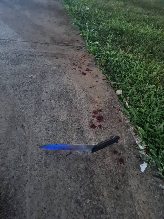 Faca de cabo preto, e lâmina aparentemente quebrada, caída em calçada com manchas de sangue