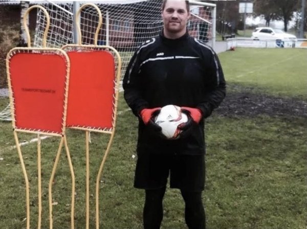 goleiro de futebol segura bola com luvas e roupa preta em um gramado