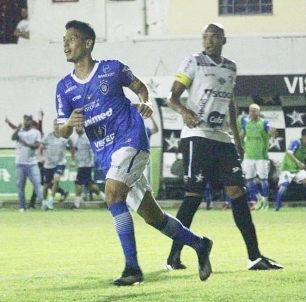 jogador de futebol com uniforme azul sai correndo ao lado de jogador de branco em um campo