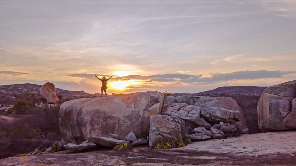 Foto colorida de um homem com os braços abertos encima de rochas