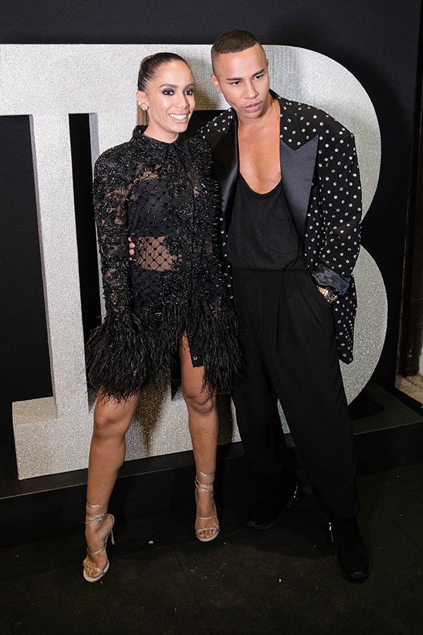 A cantora Anitta com uma roupa preta transparente posando para foto ao lado de Oliver Rousteing, estilista da marca Balmain. Ele usa blazer brilhoso com camiseta e calça preta
