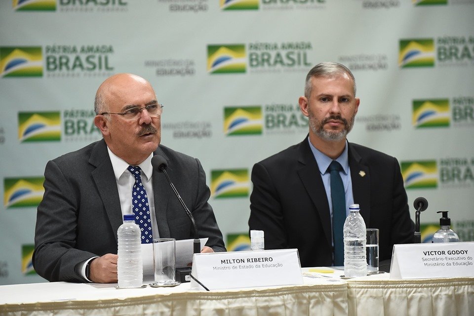 O ex-ministro da Educação ao lado do recém-batizado cargo, Victor Godoy, na época secretário.  Eles falam em coletiva de imprensa sentados em frente a mesa com microfones - Metrópoles