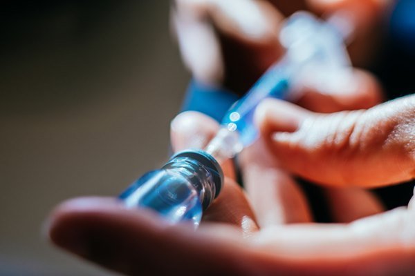Person holding syringe inside clear container with clear liquid - Metropolis