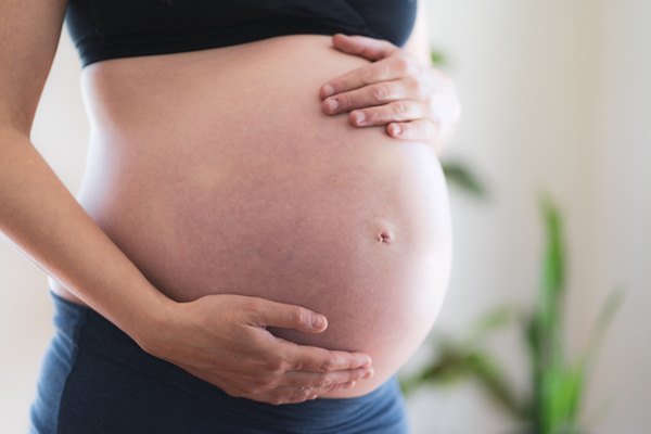 Mulher grávida com a barriga despida e com as mãos ao redor dela - Metrópoles