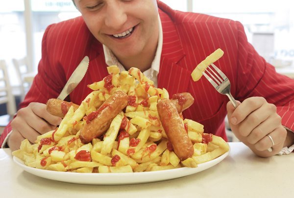 A man with a fork and knife in his hands looks at a plate of french fries - Metropoles