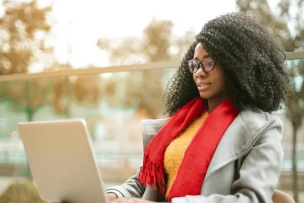 mulher negra e com os cabelos cheios e crespos trabalha ao ar livre com um computador