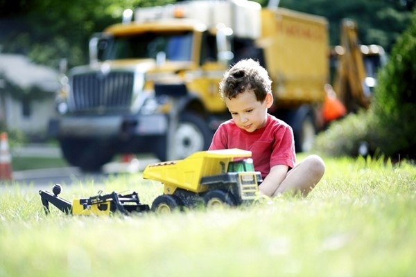 Criança sentada na grama brincando com um trator de brinquedo -metrópoles