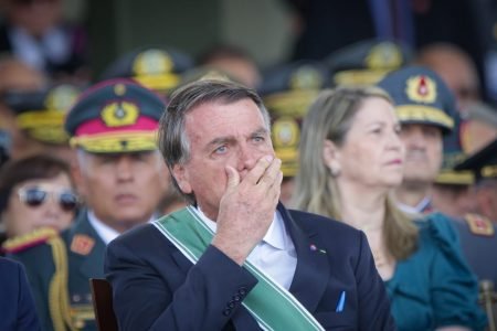 Bolsonaro olha emocionado para frente, sentado próximo a vários militares e leva a mão a boca na cerimônia militar em comemoração ao Dia do Exército, marcando os 374 anos da instituição - Metrópoles