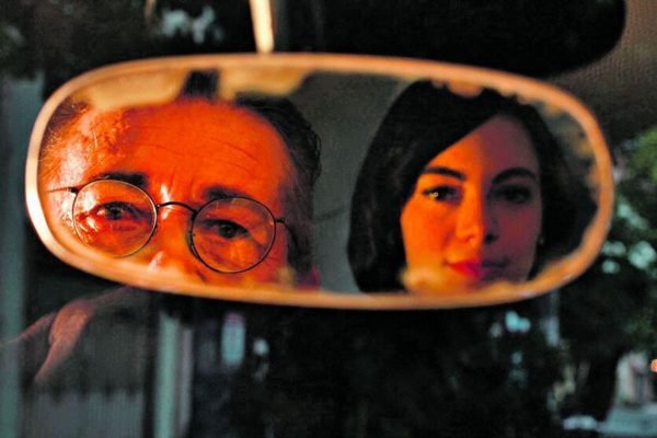 foto de duas pessoas, um homem e uma mulher, olhando pelo retrovisor interno de um carro