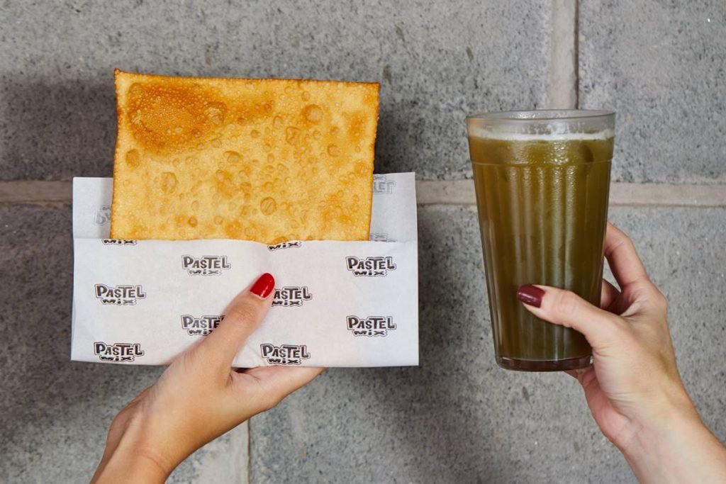 foto de mãos segurando um pastel e um copo de caldo de cana