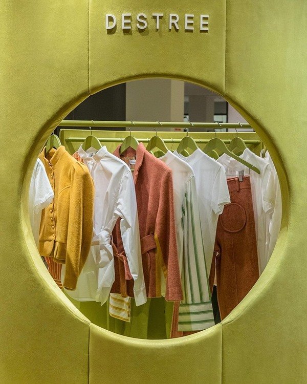 Loja de roupas com araras e cabides com peças penduradas. As roupas são brancas, rosas e amarelas 