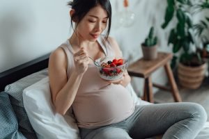 Mulher asiática grávida sentada e comendo frutas