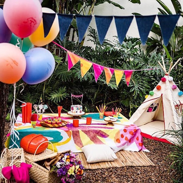 Festa de aniversário de criança com mesa de doces e bolos, bandeirinhas de decoração e uma barraca para as crianças brincarem