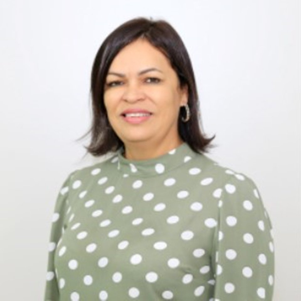Mulher com blusa cinza com bolinhas brancas, cabelo curto e sorrindo em frente a parede branca