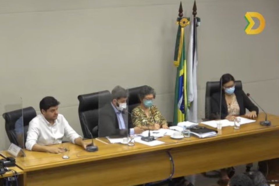 Pessoas sentadas em mesa de madeira e bandeira do Brasil ao fundo