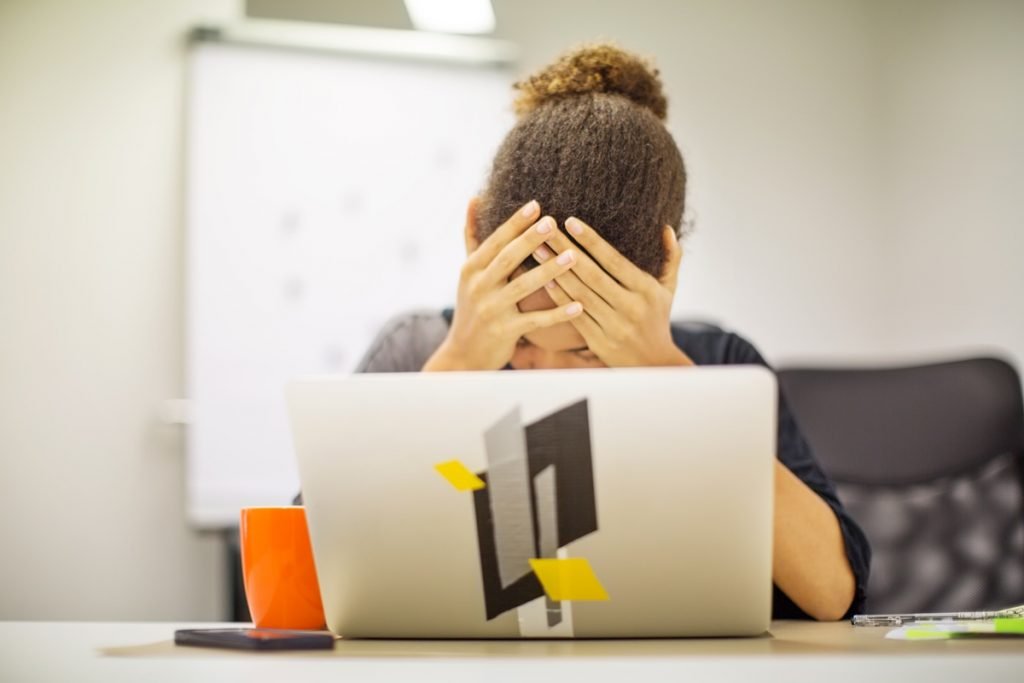 mulher negra coloca as mãos na cabeça em frente a um computador em sinal de preocupação