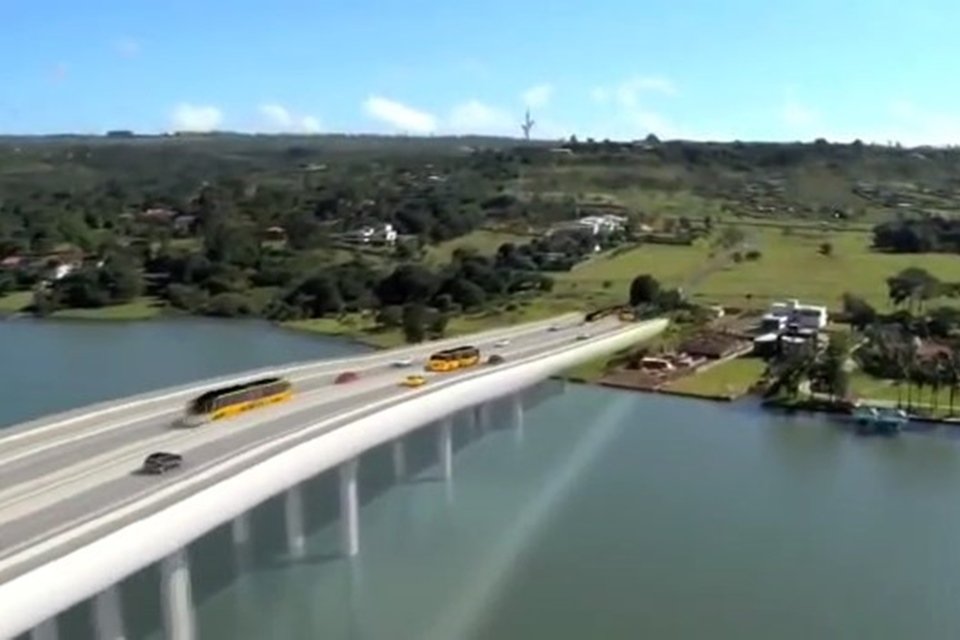 Ponte sobre lago com carros passando e gramado ao fundo