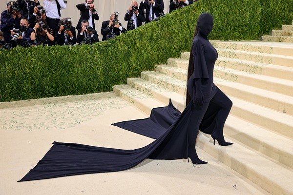 A empresária Kim Kardashian subindo as escadas do Met Gala. Ela usa um vestido preto, com cauda preta, e até uma máscara preta que cobre seu rosto e a deixa irreconhecível.
