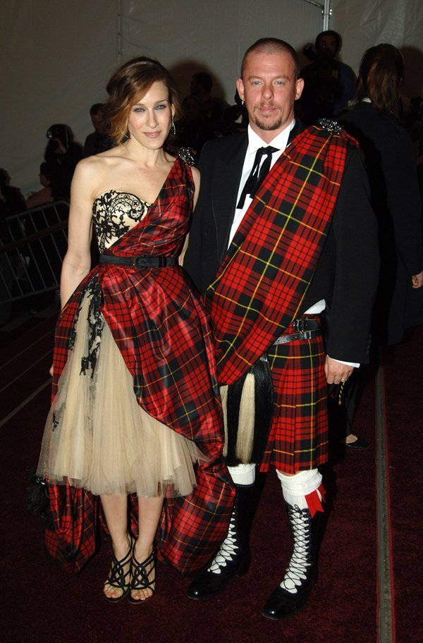 A atriz Sarah Jessica Parker e o estilista Alexander McQueen no baile do Met Gala de 2006. Ela usa um vestido bege de tule, com bustiê preto de renta, e uma faixa de tecido xadrez. Ele usa uma camisa branca, um blazer preto e uma gravata. Usa, ainda, uma saia xadrez e uma faixa de tecido na mesma estampa.