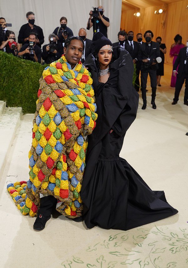 Cantora Rihanna e rapper ASAP Rocky no baile do Met Gala em 2021. Ele usa uma roupa que parece um cobertor de retalhos coloridos. Rihanna usa uma capa preta com joias prateadas e de diamantes