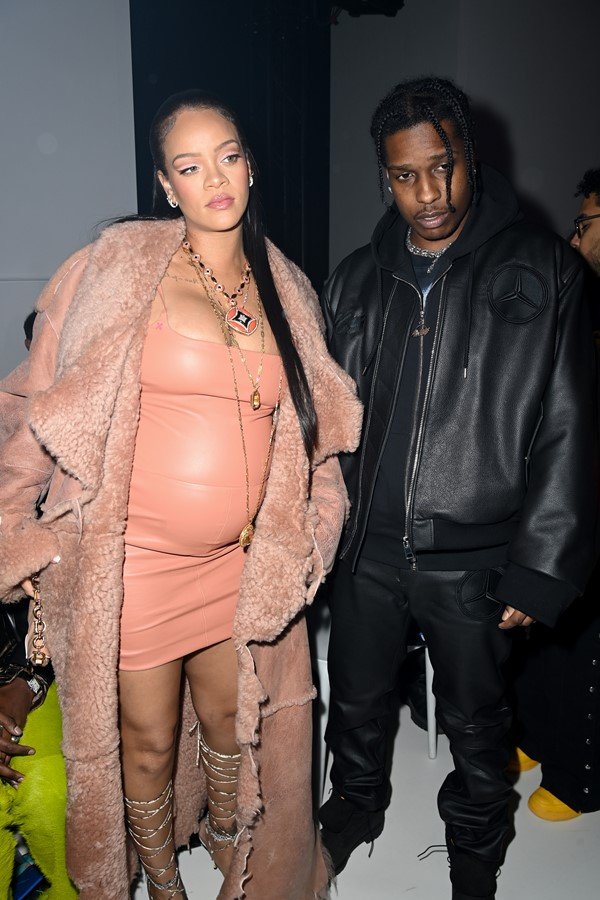 Cantora Rihanna e o namorado ASAP Rocky no desfile da Off White, em Paris, em março de 2022. Ela está grávida e usa um vestido de látex na cor salmão e um casaco de pele por cima, na cor bege. Ele usa camiseta, jaqueta e calça, tudo preto.
