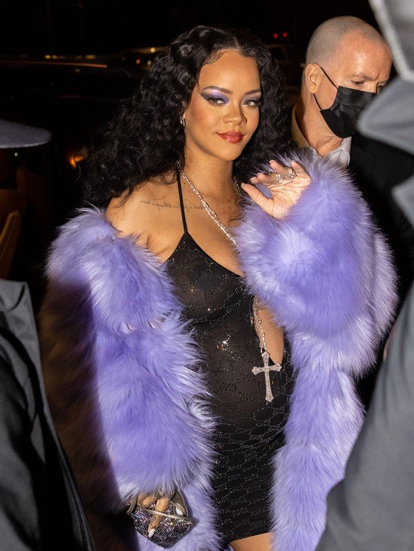 Rihanna entrando em evento. Ela usa um vestido preto justo, da marca Gucci, justo ao corpo, e um casaco lilás de pelúcia.