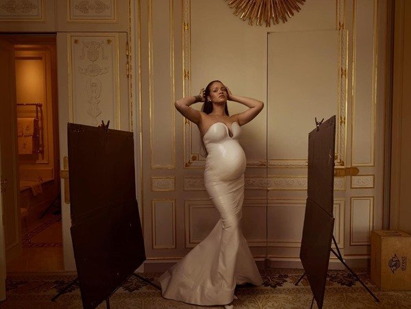 Cantora Rihanna grávida, com vestido branco colado, posando para foto no corredor de um hotel.