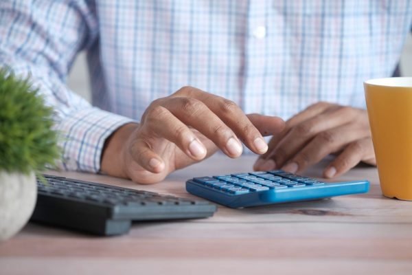 Homem usando calculadora em frente ao computador