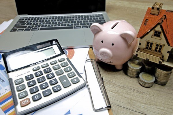 Calculadora, papeis, notebook, moedas e um cofre em formato de porco em cima de uma mesa- Metrópoles